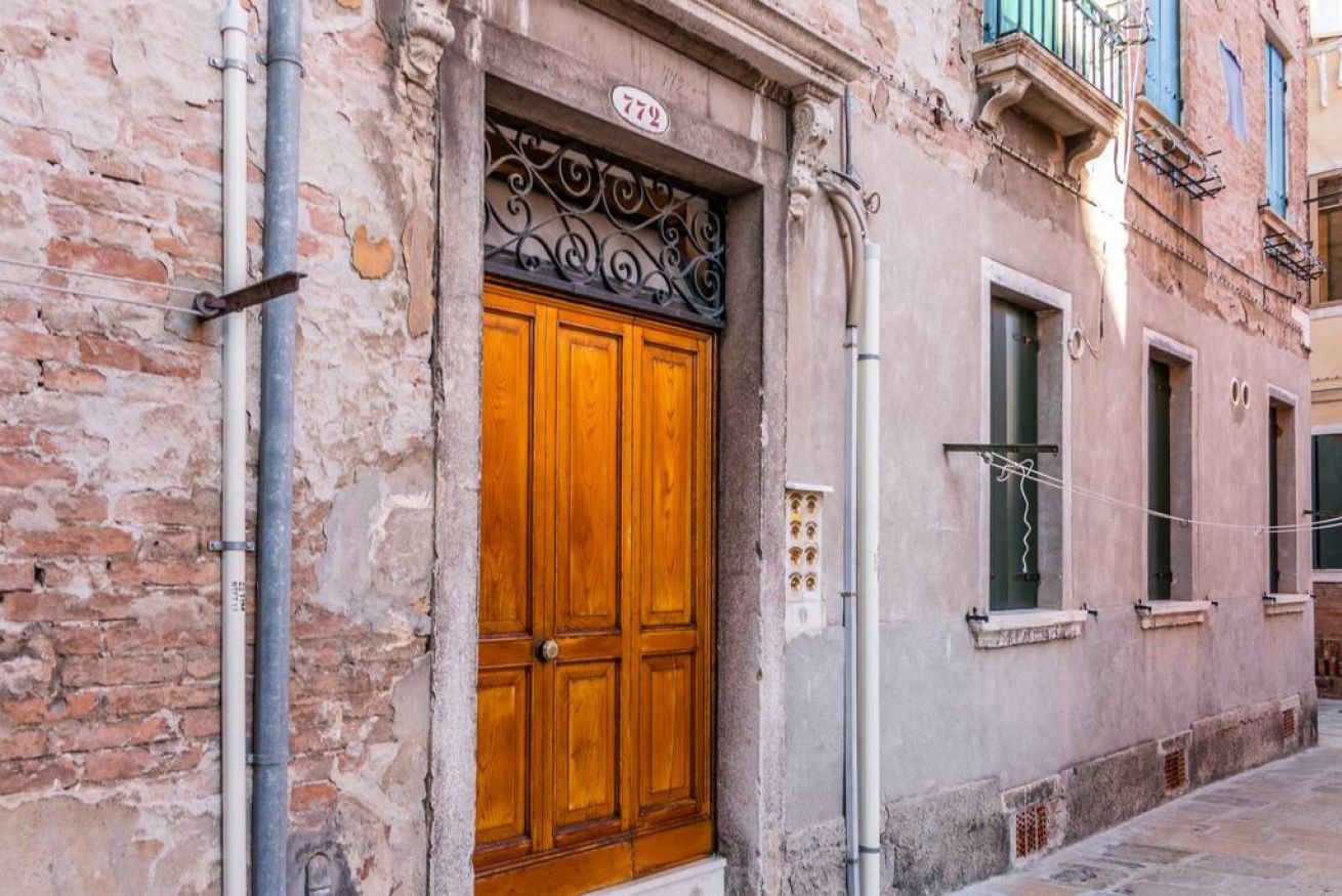 A building with a wooden door, a number plaque, and a window with a curtain.