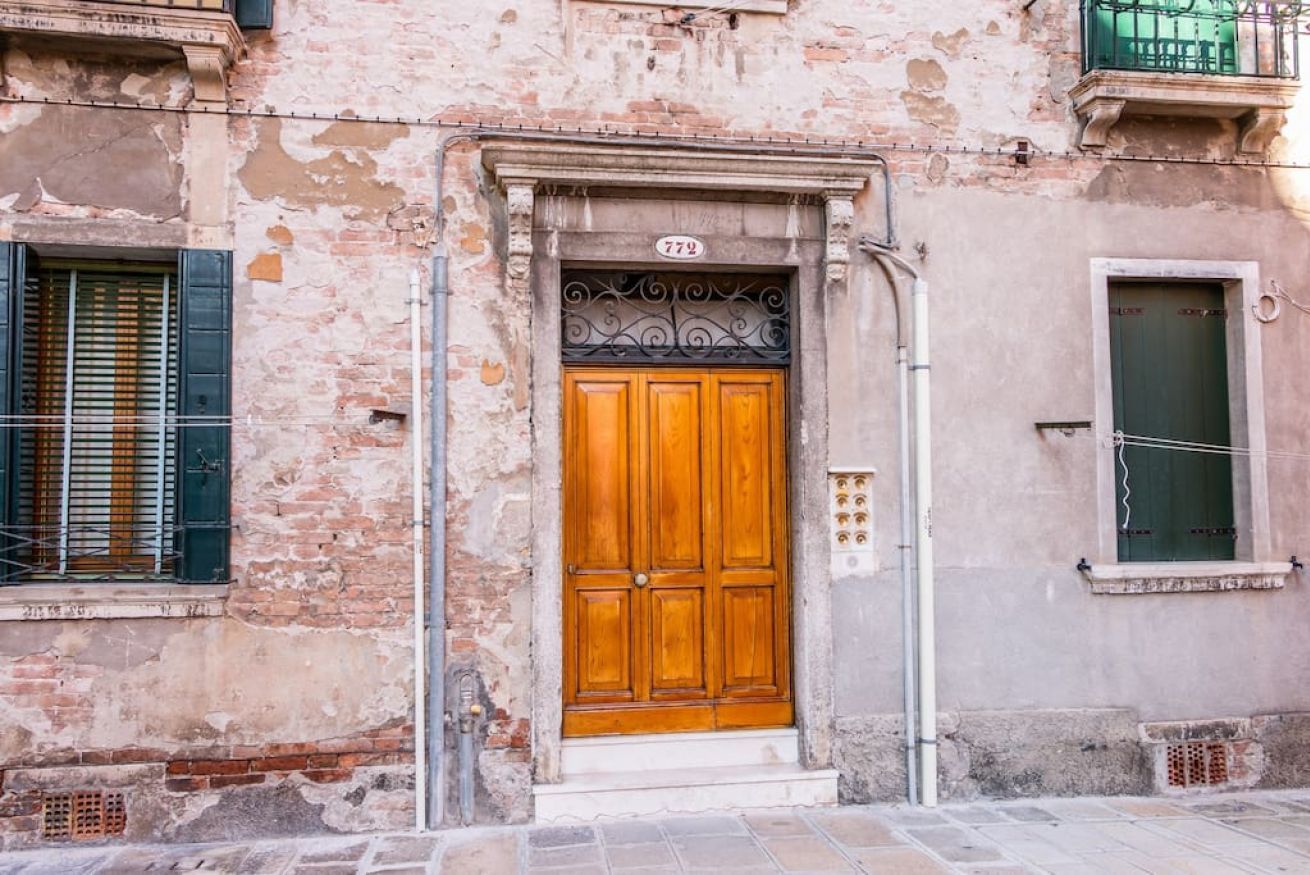 A weathered building facade with a wooden door, a window with shutters, and a balcony.