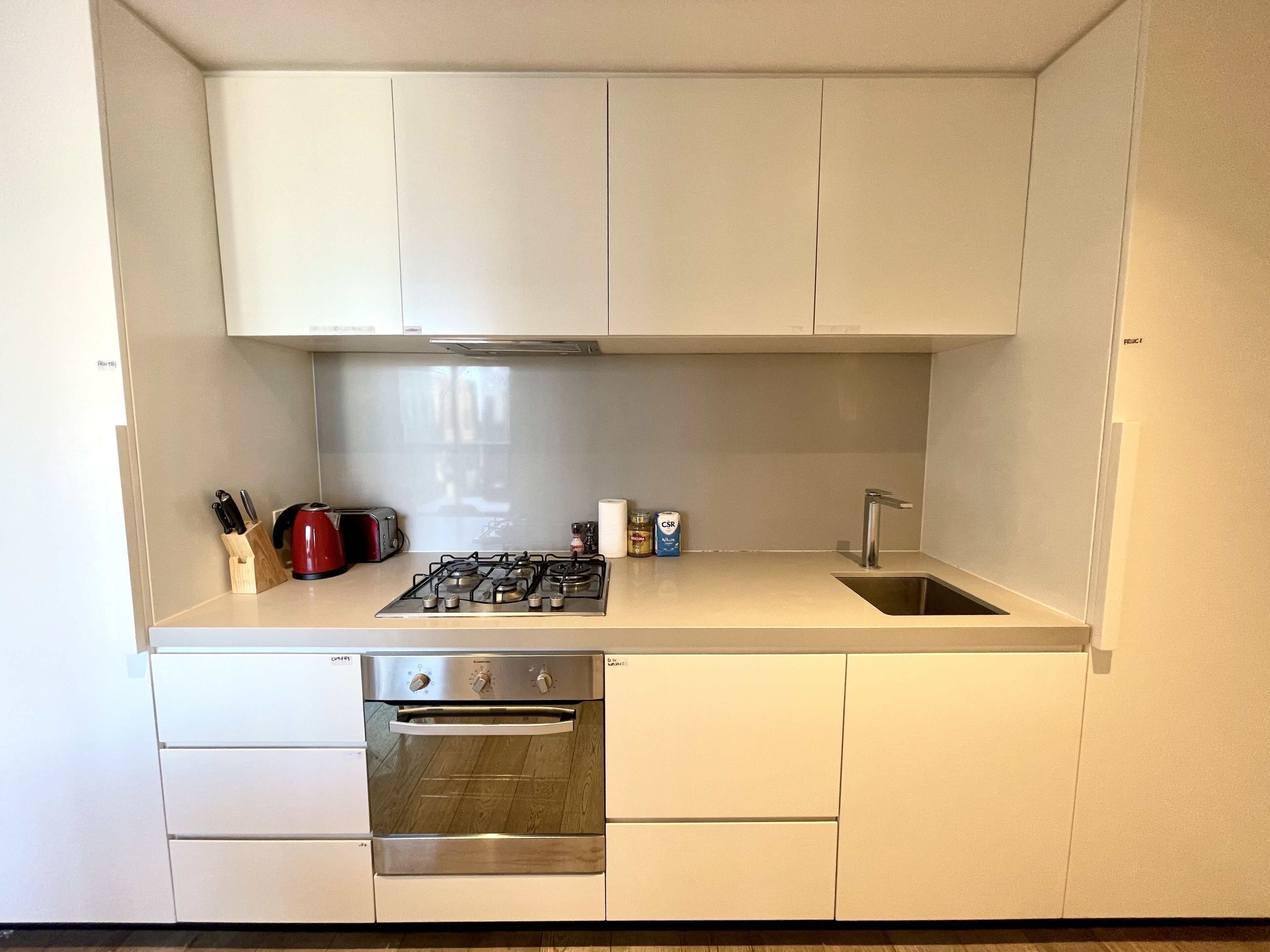 Una cucina compatta con mobili bianchi, un fornello a gas, forno integrato e lavandino.