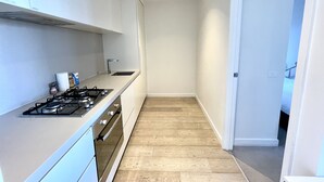 A narrow kitchen with white cabinets, a gas stove, and a wooden floor. - Readyset Apartments at Empire (Melbourne)