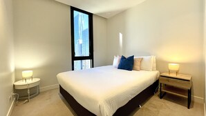 A modern hotel room with a large bed, a bedside table, and a nightstand. - Readyset Apartments at Empire (Melbourne)