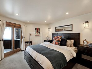 A bedroom with a large bed, a sliding glass door, a bedside table with a lamp, and a wall-mounted artwork. - Spacious mountain retreat • Built for gathering • Hot tub • Quiet setting • Minutes up Sundance Canyon (Sundance)