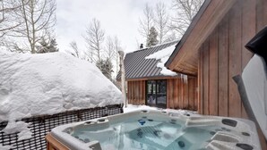 Un jacuzzi en un área exterior nevada, con un edificio de madera al fondo.