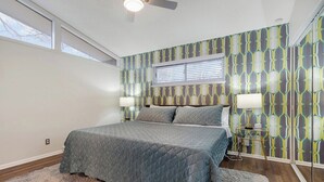 Quarto com cama, duas mesas de cabeceira, ventilador de teto e papel de parede estampado.