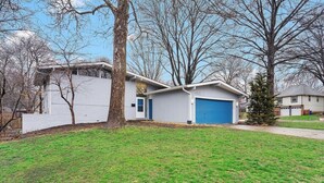 Uma casa residencial com garagem, jardim frontal e uma árvore.