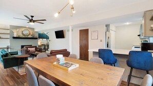 Uma sala de estar moderna com uma mesa de jantar de madeira, cadeiras azuis, um ventilador de teto e uma lareira.