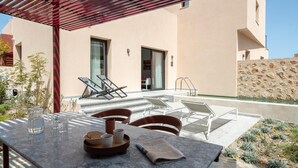 Um terraço com mesa, cadeiras, jarra de água, copos e um jornal.