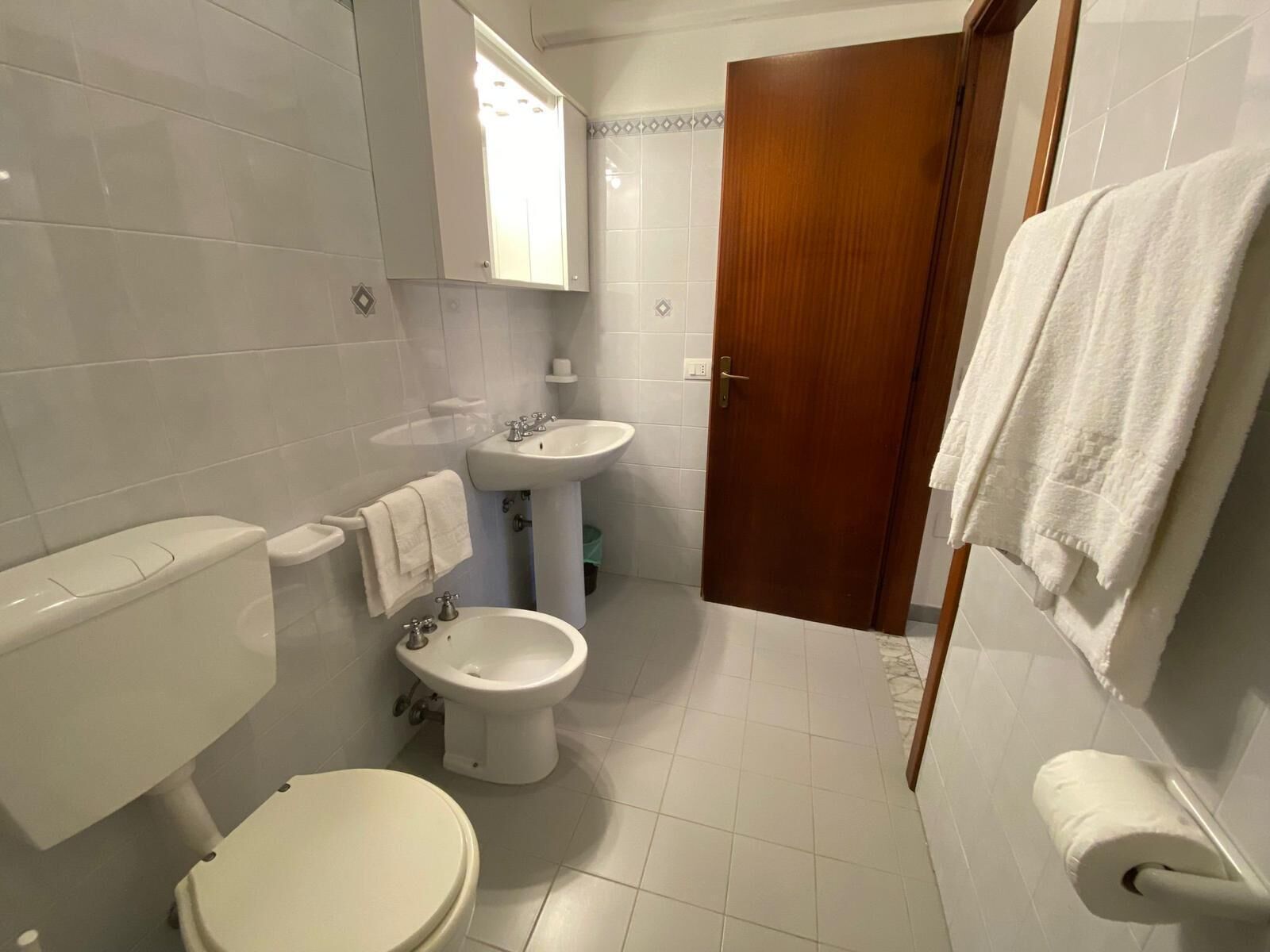 Een badkamer met toilet, bidet, wastafel en spiegel.