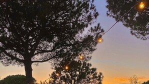 An outdoor seating area with a wooden table and cushions, surrounded by trees and string lights. - Hibiscus Beach Village - Family apartments within walking distance of the sea (Follonica)