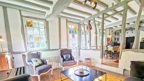 A cozy living room with a fireplace, wooden beams, and a dining area with a table and chairs. - Le Nid de Chaume, 15 min from Honfleur 4/6P Charming little cottage, (Martainville)