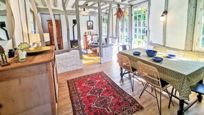 A rustic kitchen with exposed beams, a brick wall, and a dining area with wicker chairs and a patterned tablecloth. - Le Nid de Chaume, 15 min from Honfleur 4/6P Charming little cottage, (Martainville)