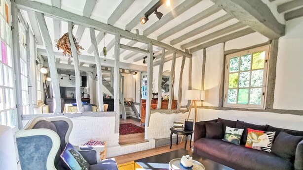 A cozy living room with a sofa, armchair, and coffee table. A staircase leads to an upper level, and a window provides natural light. - Le Nid de Chaume, 15 min from Honfleur 4/6P Charming little cottage, (Martainville)