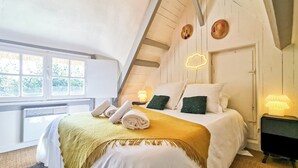 A cozy bedroom with a sloped ceiling, a bed with white linens, green pillows, and a yellow throw blanket. There are two bedside lamps and a wall-mounted light fixture. - Le Nid de Chaume, 15 min from Honfleur 4/6P Charming little cottage, (Martainville)