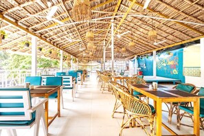 An open-air restaurant with thatched roofs, wooden tables, and blue chairs. - Casanova by the Sea (Canacona)