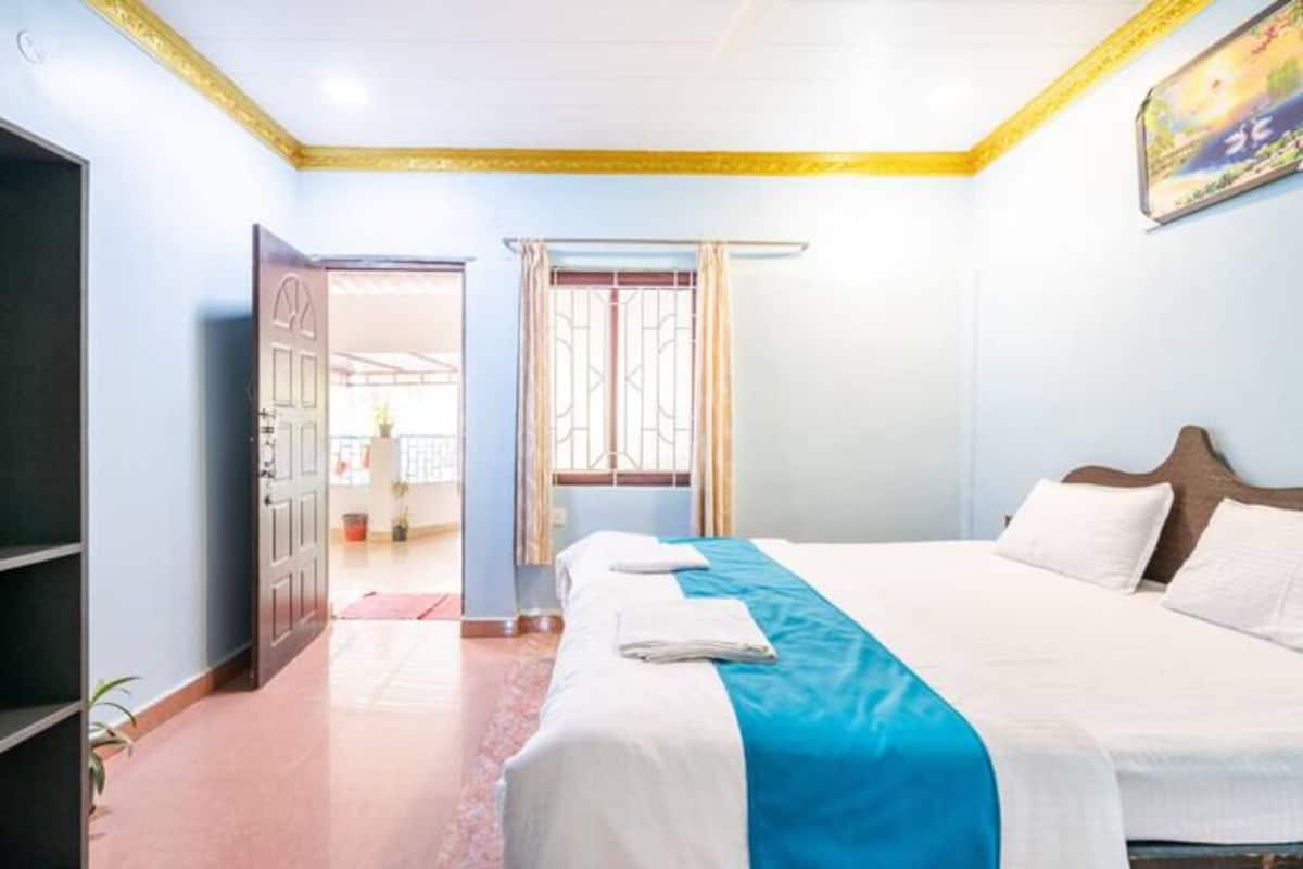 Una habitación de hotel con cama, una puerta, ventana con cortinas y un cuadro en la pared.