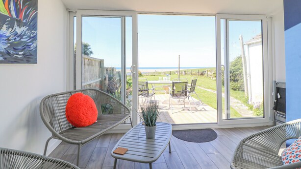 Eine geräumige Terrasse mit Korbstühlen, einem Tisch und Blick aufs Meer.
