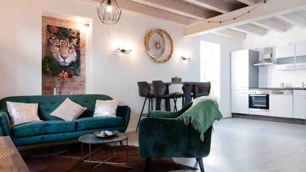 Un salon moderne avec un canapé turquoise, un fauteuil vert et un coin repas doté d’une table ronde.