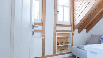 A room with a sloped ceiling, built-in shelves, a radiator, and a white sofa.