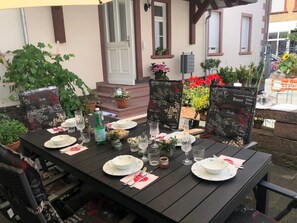 Ein Essbereich im Freien mit einem Tisch für vier Personen, umgeben von Topfpflanzen und Blumen.