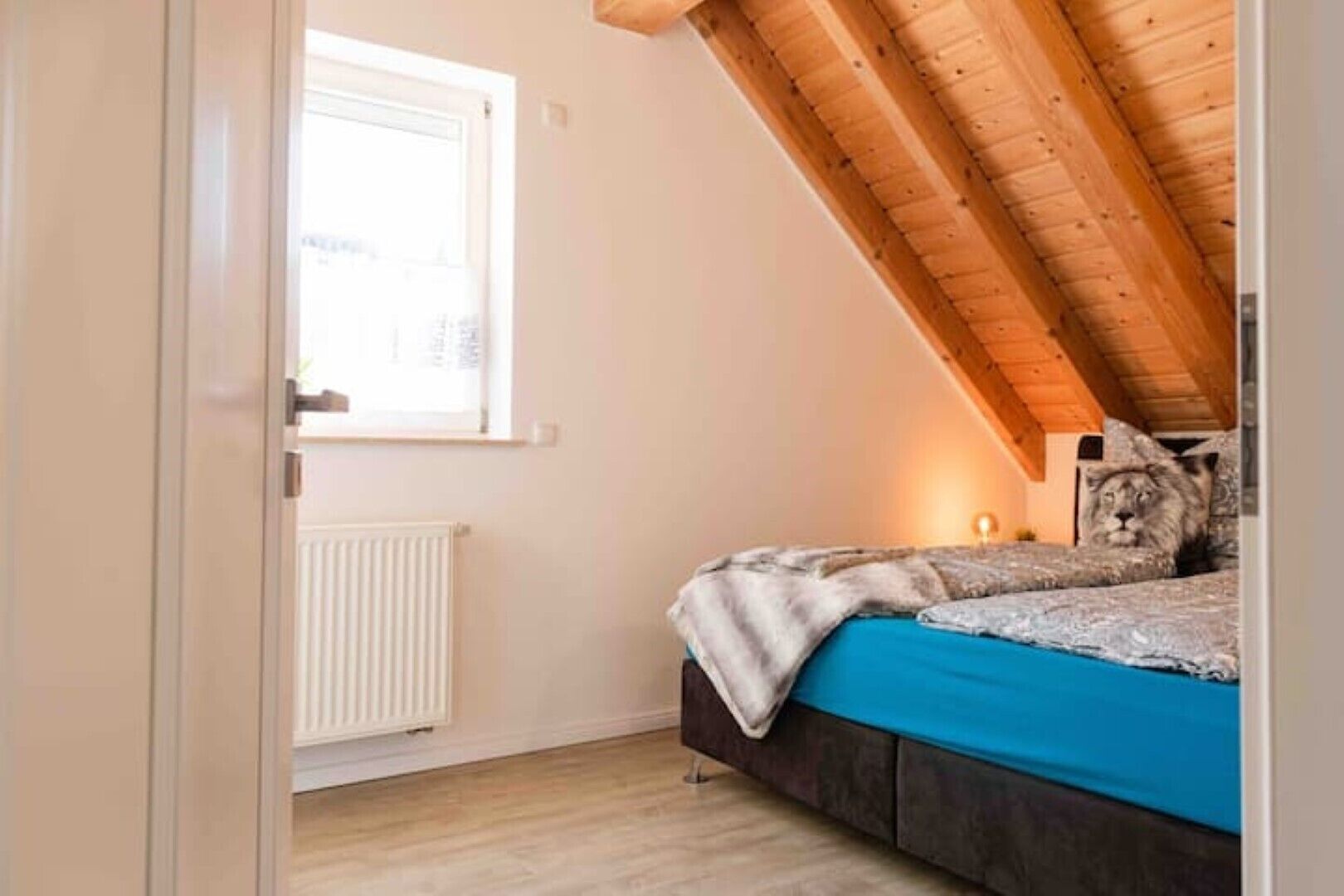 A bedroom with a sloped ceiling, a window, a radiator, and a bed with a blue bedspread.