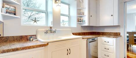 A kitchen with white cabinets, a granite countertop, a built-in dishwasher, and a window with a starfish decoration.