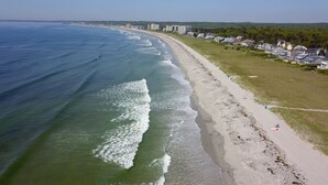 Una spiaggia costiera con un litorale sabbioso, una zona erbosa con case e una vista libera sull'oceano.