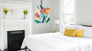 Una camera da letto con un letto bianco, un camino e un dipinto di fiori.