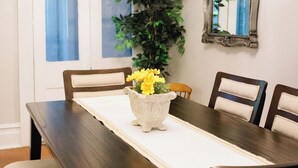Un'area pranzo con un lungo tavolo di legno, quattro sedie, un vaso con fiori gialli e uno specchio appeso al muro.