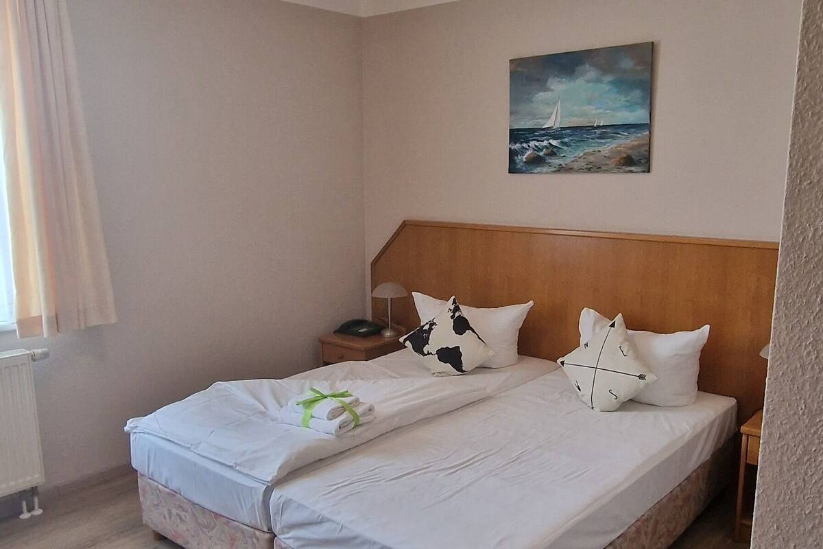 Une chambre d’hôtel avec un lit, un tableau au mur et une fenêtre avec des rideaux.