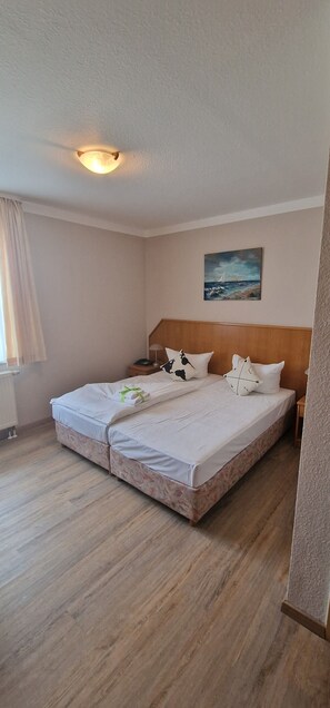 Una habitación de hotel con cama, un cuadro en la pared y una ventana con cortinas.