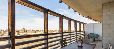 A balcony with a view of the city, a table with chairs, and a hanging lantern.