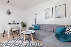 A modern living room with a grey sofa, teal cushions, a patterned rug, a dining table with chairs, and two abstract paintings on the wall. - Family Apartment in Gdynia | Balcony | Close to Station (Gdynia)