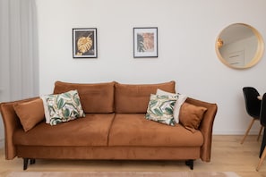 A brown sofa with two patterned pillows, a round mirror, and two framed pictures on the wall.