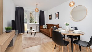 Una sala de estar moderna con un sofá marrón, una mesa de comedor dispuesta con platos y vasos, y un espejo grande en la pared.