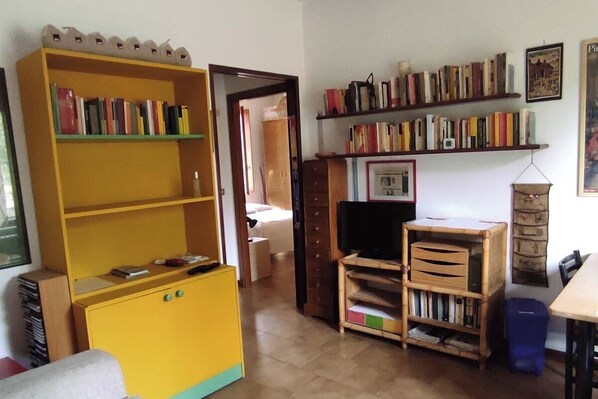 Een kamer met een geel boekenrek, een televisie en een houten kast met lades.