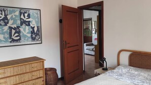 Une chambre à coucher comprenant un lit, une commode, une porte donnant sur une autre pièce et un mur orné d’un tableau encadré.