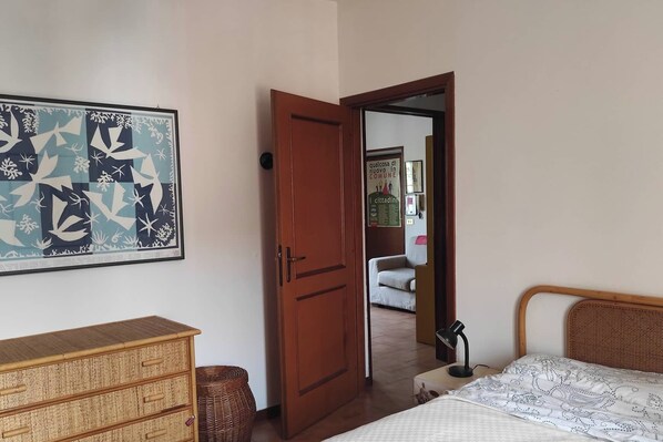 Une chambre à coucher comprenant un lit, une commode, une porte donnant sur une autre pièce et un mur orné d’un tableau encadré.
