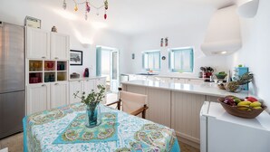 A modern kitchen with white cabinetry, a dining table with a colorful tablecloth, and a fruit bowl on the counter.