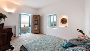 A bedroom with a bed, a wooden wardrobe, a window with a view, and a wall-mounted light fixture.