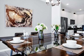 Un espace repas moderne avec une table en verre, de l’assiette blanche et des vases remplis de fleurs blanches.