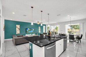 A modern kitchen with a central island, a dining area with a table and chairs, a sofa, and a TV on the wall.