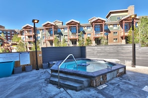 Un bain à remous doté d’une terrasse en bois et d’escaliers, entouré d’une piscine, avec une pancarte indiquant une capacité maximale de 18 personnes.