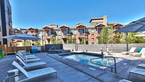 A pool area with lounge chairs and umbrellas, surrounded by multi-story buildings with balconies.