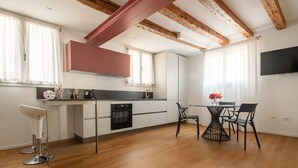 A modern kitchen with wooden beams, a dining area with a table and chairs, and a TV mounted on the wall.