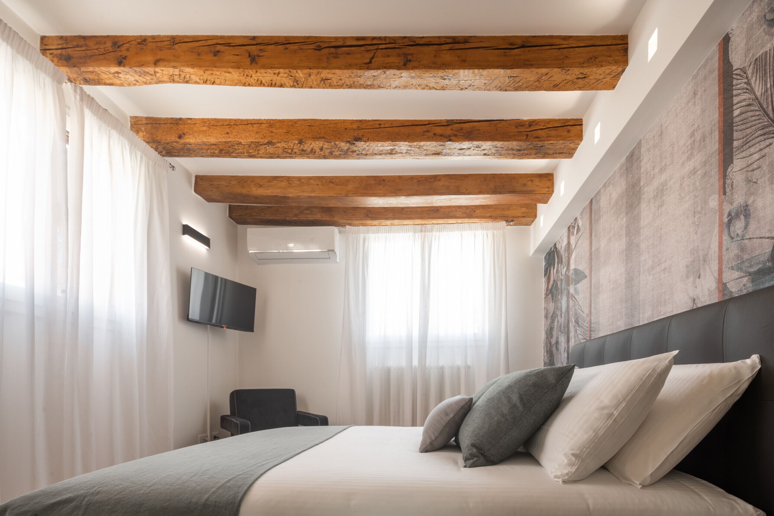 Ein Schlafzimmer mit einem Bett, Holzbalken, einem Flachbildfernseher und einem großen, abstrakten Gemälde an der Wand.