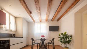 A modern kitchen with wooden beams, a dining table with chairs, a potted plant, and a TV on the wall.