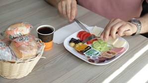 Eine Mahlzeit mit Brot, Käse, Oliven, Tomaten, Gurken und einer Tasse Kaffee auf einem Tisch.