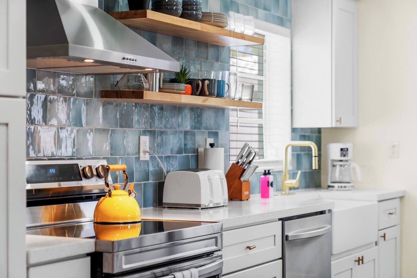 Una cocina moderna con campana extractora de acero inoxidable, un hervidor amarillo, un tostador y una cafetera.