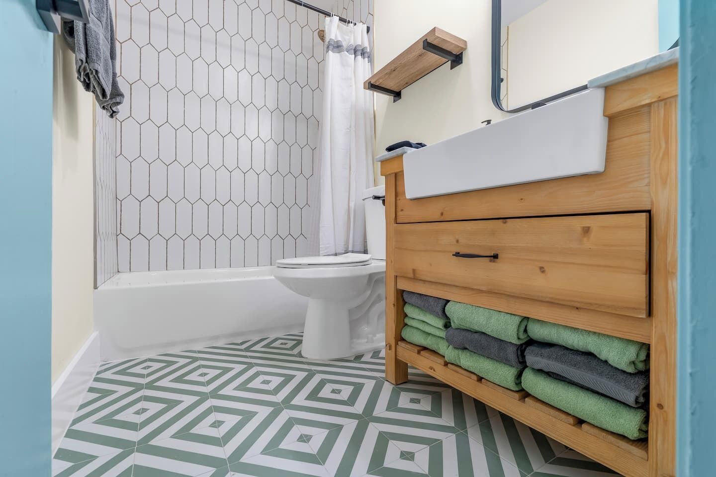 A bathroom with a white toilet, a wooden cabinet with towels, and a hexagonal patterned shower enclosure.