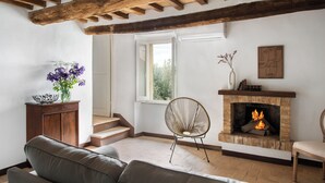 A living room with a fireplace, wooden beams, a sofa, and a chair. - Il Borghetto - The House of Elba, rooftop panoramic terrace (Castelnuovo dell'Abate)